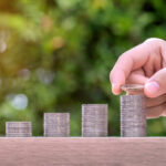 Hand holding coin and stack of money on wood table. Pension fund concept.