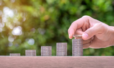 Hand holding coin and stack of money on wood table. Pension fund concept.
