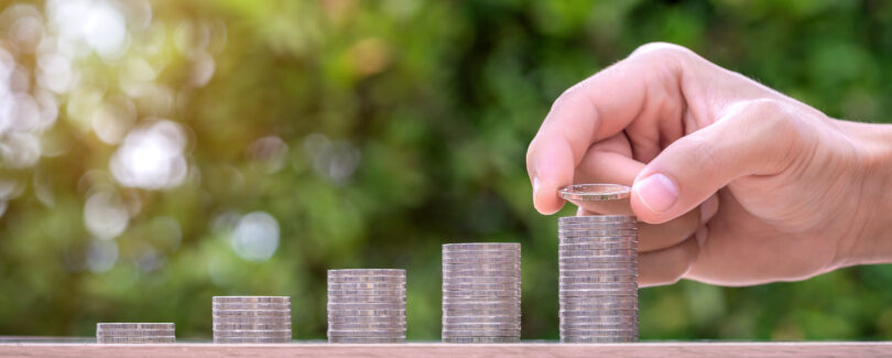 Hand holding coin and stack of money on wood table. Pension fund concept.